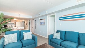 A modern living room with two blue sofas, a dining area, and a kitchen. - Salty Air & Sunset Chairs | Bayfront Bliss in OCMD (Ocean City)