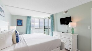 A hotel room with a bed, a dresser, a TV mounted on the wall, and a window with curtains. - Fries, Ferris Wheels & Bay Views | Your OCMD Getaway (Ocean City)