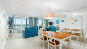A modern living room with a blue sofa, white chairs, and a wooden dining table. - Crab Feast Headquarters | Bay Views & Beach Days Await (Ocean City)