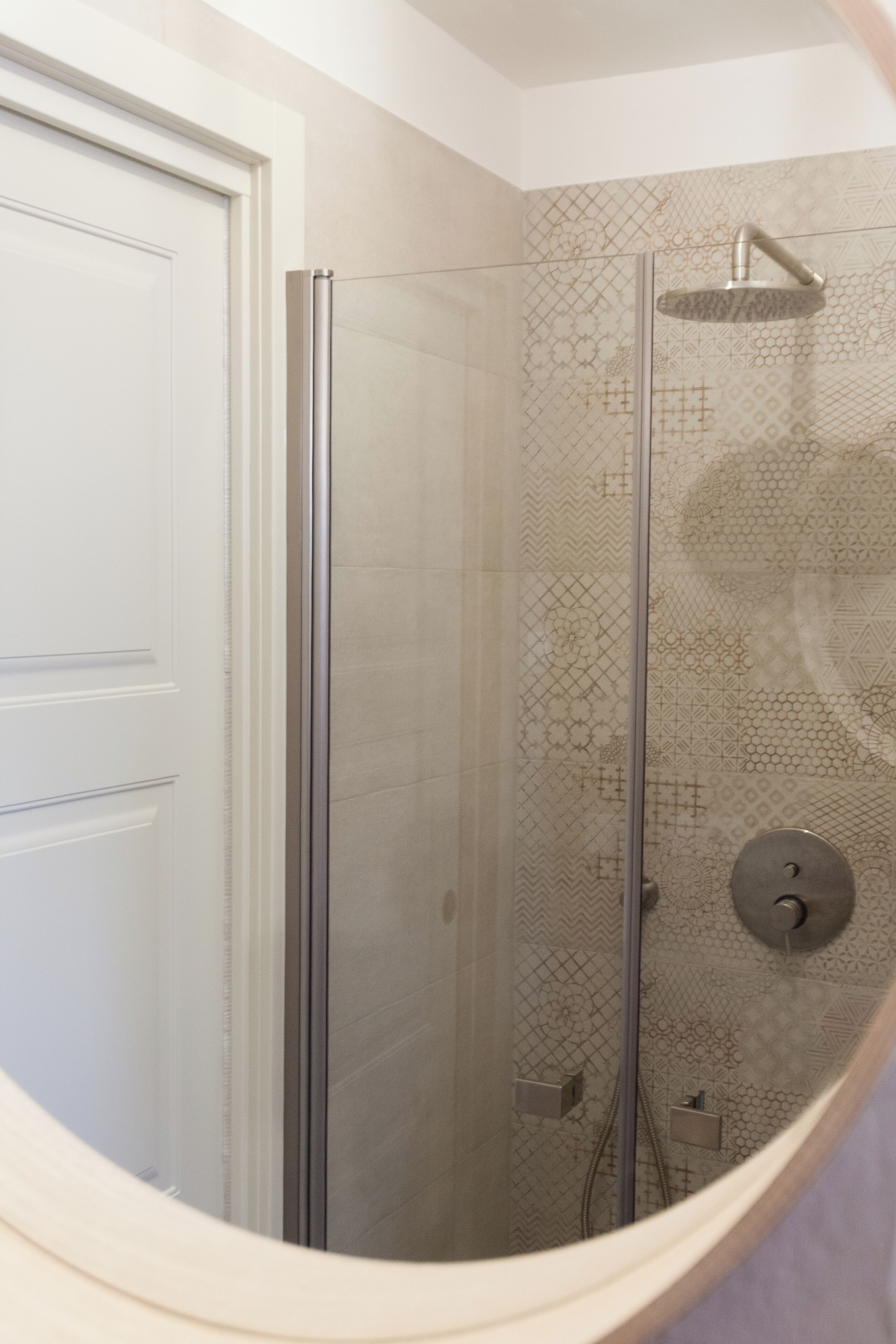 A shower with a glass door and a patterned tile wall.