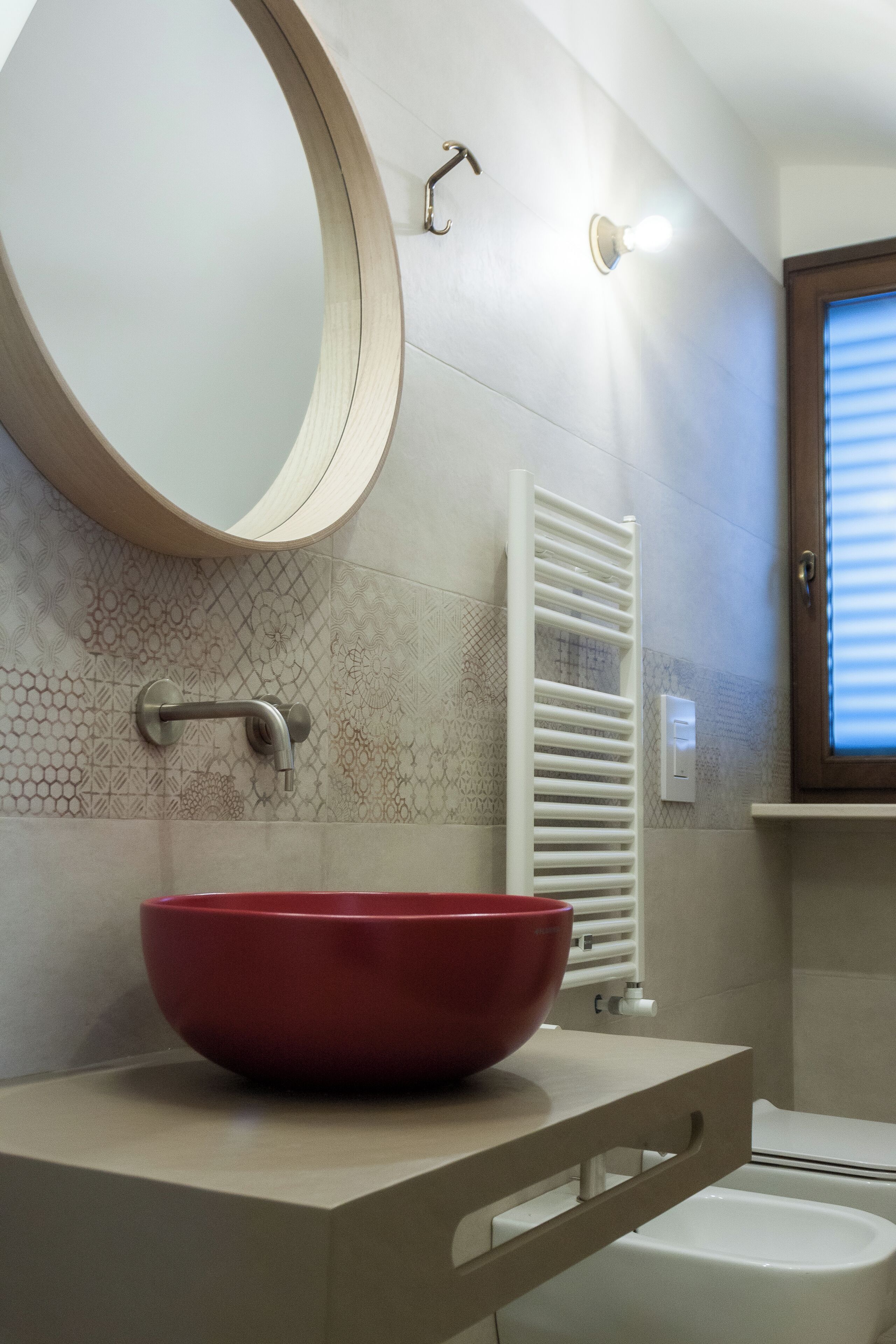 A bathroom with a round mirror, a red basin, a white radiator, and a toilet.