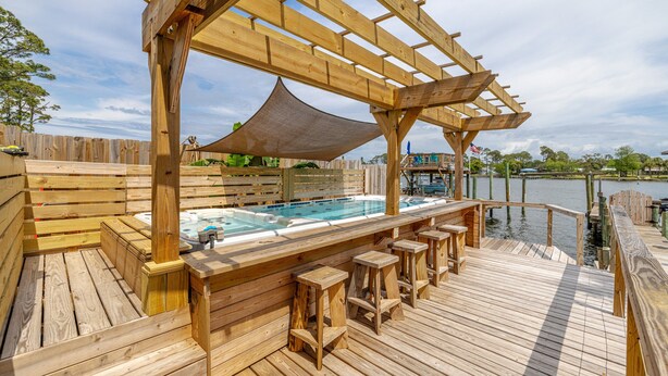 A wooden deck with a hot tub and bar stools, overlooking a body of water.