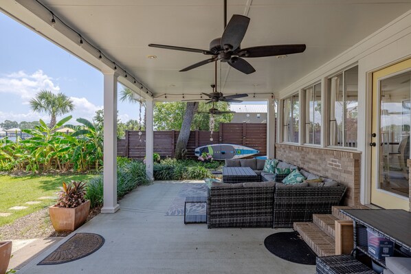 A covered patio area with a ceiling fan, outdoor seating, and a surfboard leaning against a fence. - Driftwood, jet ski pad, boat dock! (Panama City)