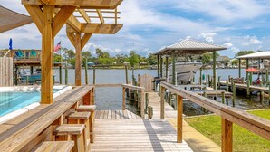 A wooden deck with a pool, a gazebo, and a dock with boats.