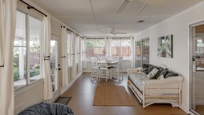 A spacious room with a dining area, a white wicker sofa, and large windows.