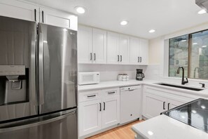 A modern kitchen with white cabinets, stainless steel appliances, and a window providing natural light.