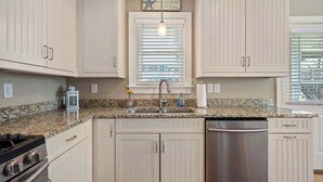 A kitchen with white cabinets, a granite countertop, a stainless steel dishwasher, and a gas stove.