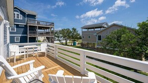A wooden deck with white chairs, a balcony, and a view of neighboring houses.