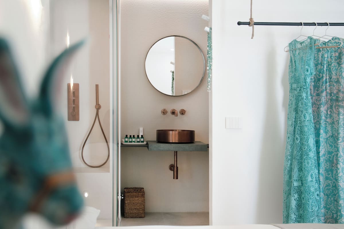 A bathroom with a round mirror, copper sink, and a hanging towel rack.