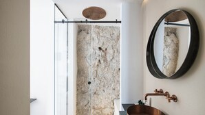 Een moderne badkamer met een glazen douchecabine, een koperen wastafel en een grote spiegel.