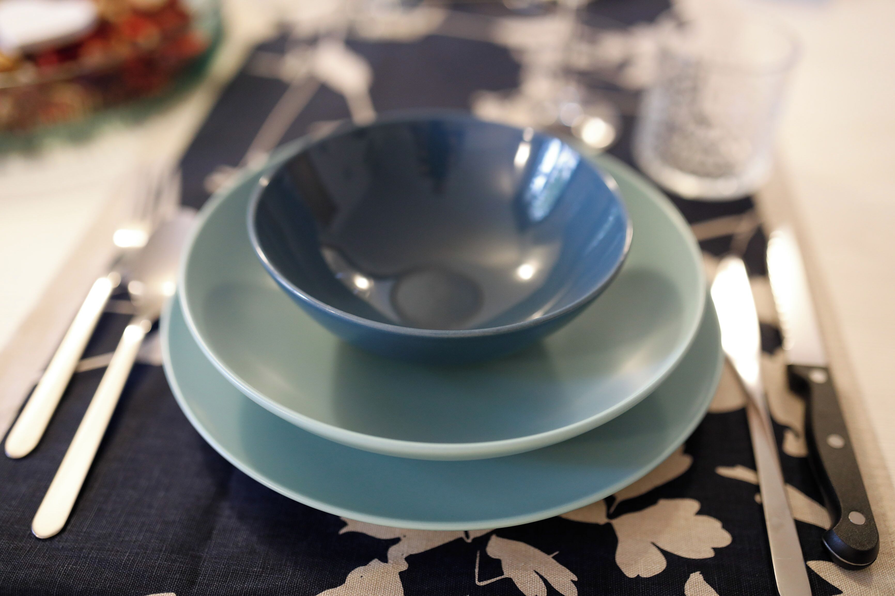 A table set with a blue bowl, a knife, and a fork on a tablecloth with a black and white pattern.