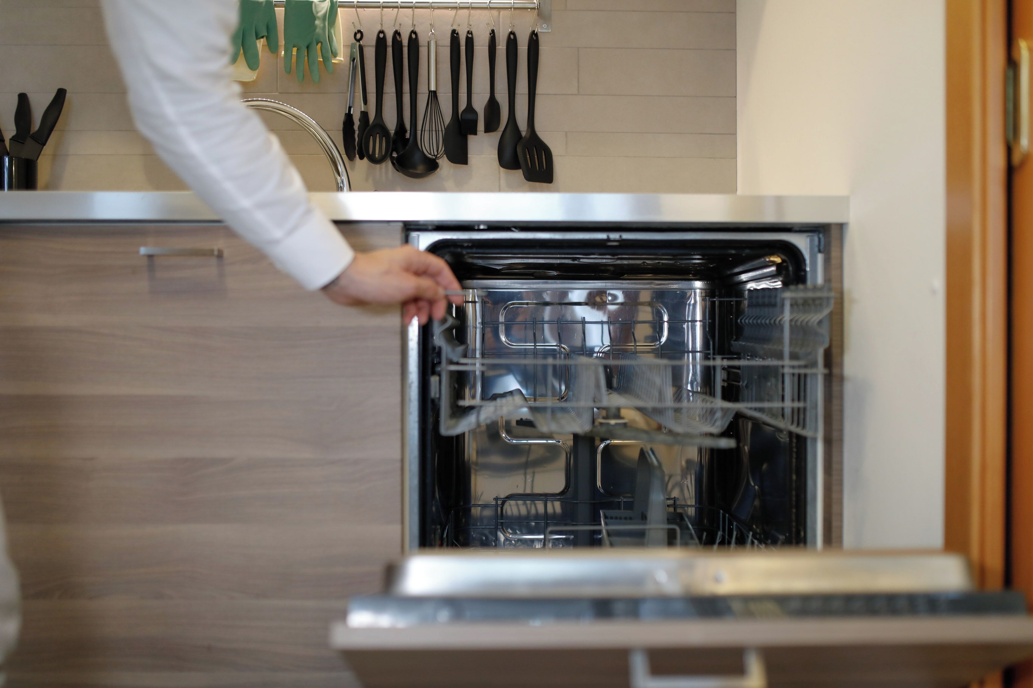 Une cuisine équipée d’un lave-vaisselle, de meubles en bois et de divers ustensiles de cuisine accrochés au mur.