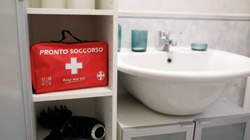 Ein Badezimmer mit einem weißen Waschbecken, einer roten Erste-Hilfe-Ausrüstung mit dem Aufdruck "PRONTO SOCCORSO" und einem Fön auf dem Regal.
