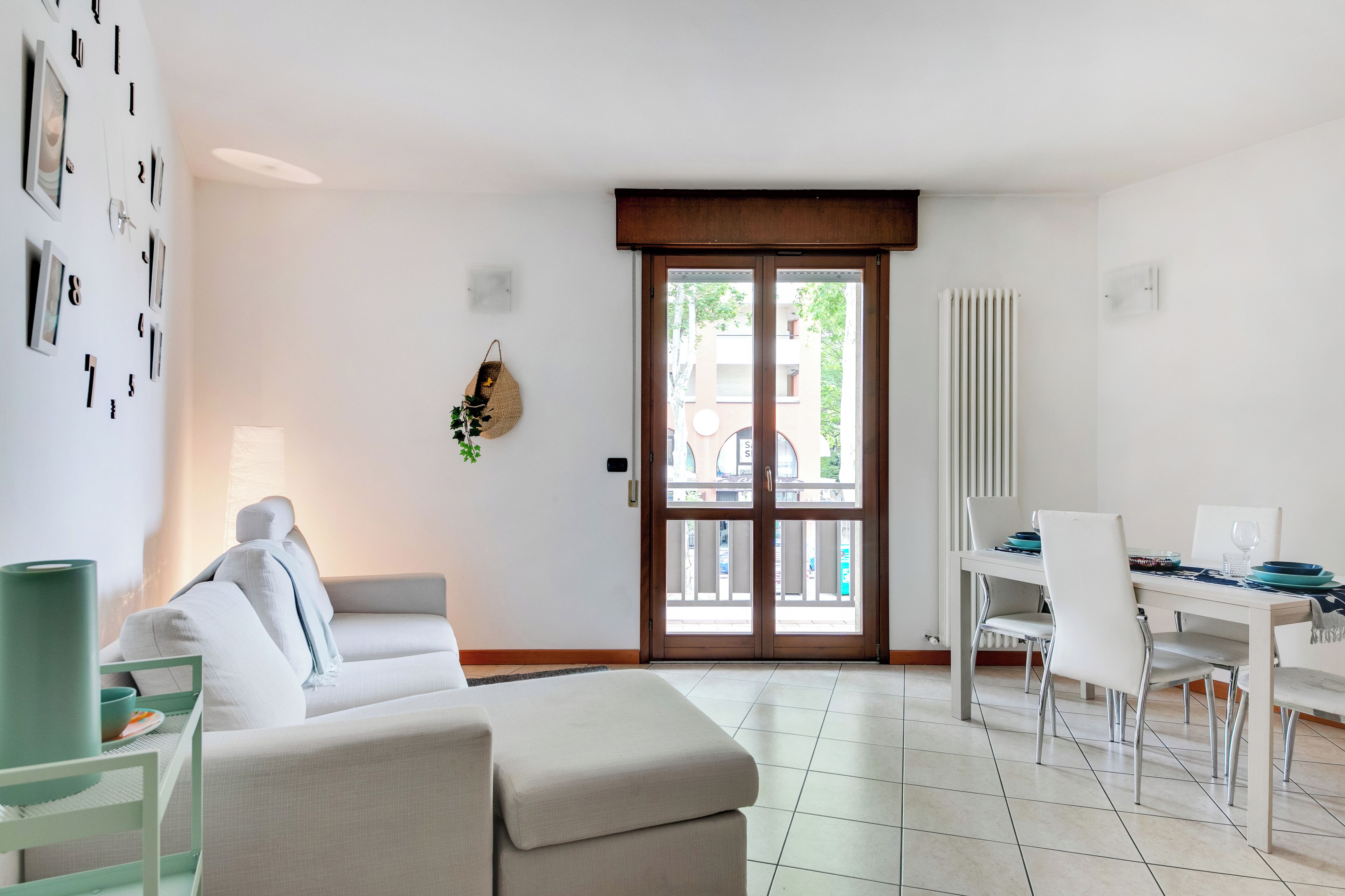 A modern living room with a sofa, a dining table with chairs, and a view through a glass door.