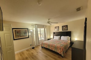 A bedroom with a bed, a ceiling fan, a window with curtains, and a door.