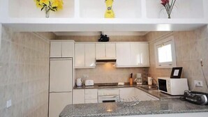 A kitchen with white cabinets, a granite countertop, a microwave, and a small refrigerator. - Villa Violeta with electrically heated pool (Puerto del Carmen)