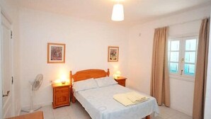 A bedroom with a bed, bedside lamps, a fan, and a window with curtains. - Villa Violeta with electrically heated pool (Puerto del Carmen)