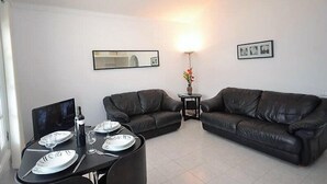 A living room with a black leather sofa, a dining table set with plates and glasses, and a small side table with a vase. - Villa Violeta with electrically heated pool (Puerto del Carmen)