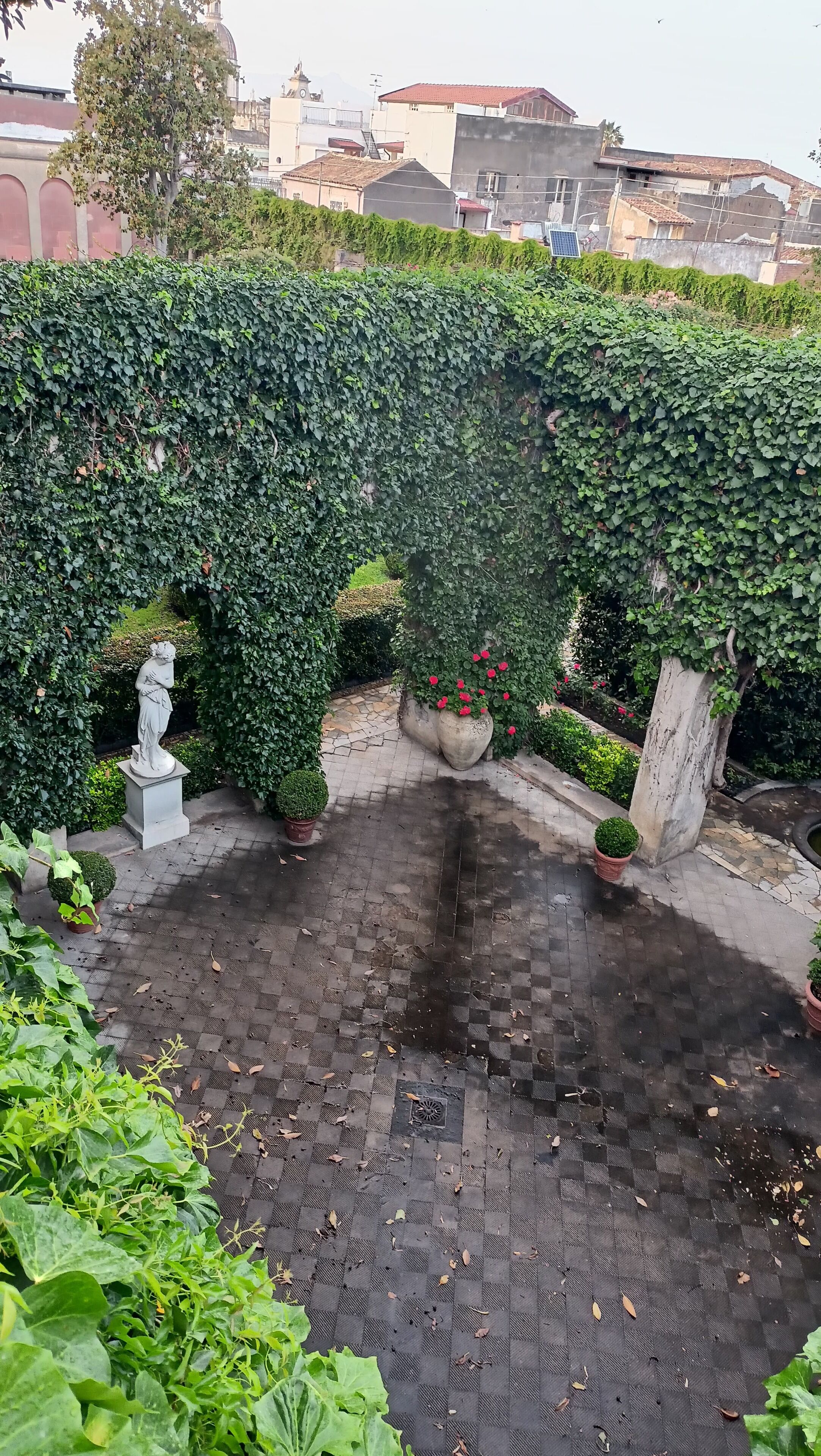 Ein Innenhof mit Schachbrettmuster, umgeben von üppigem Grün und einer Statue.