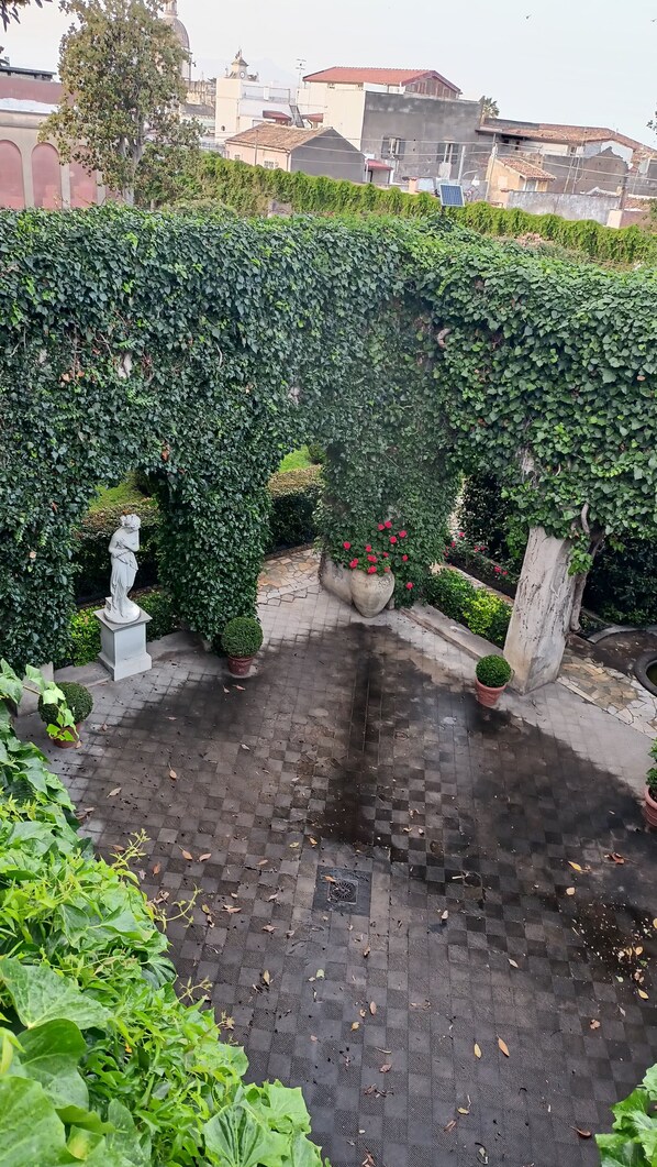 A courtyard with a checkered floor, surrounded by lush greenery and a statue. - At home "at Marco's" (Riposto)