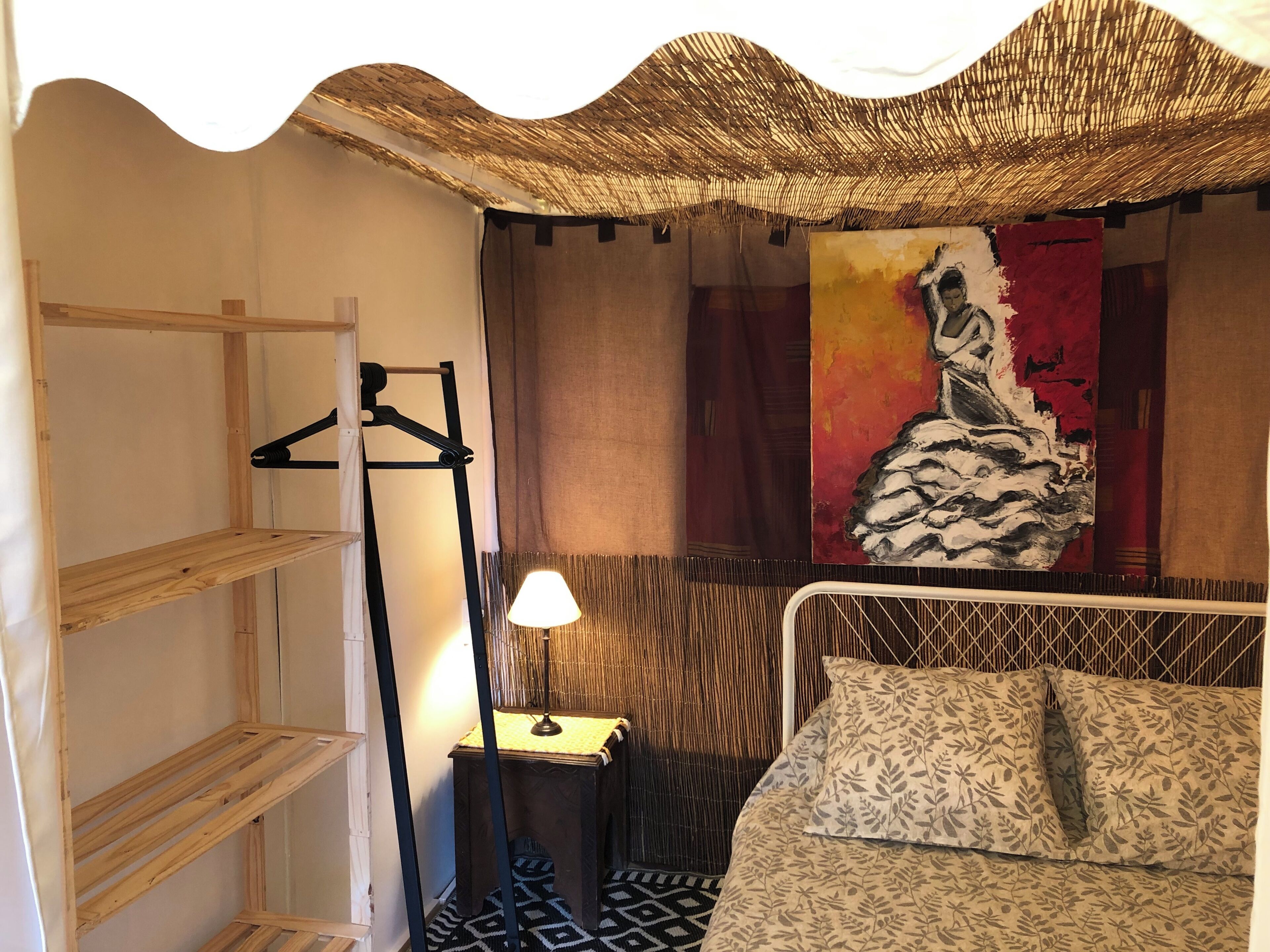 Une pièce comprenant un lit, un portant à vêtements, une lampe et un tableau accroché au mur.
