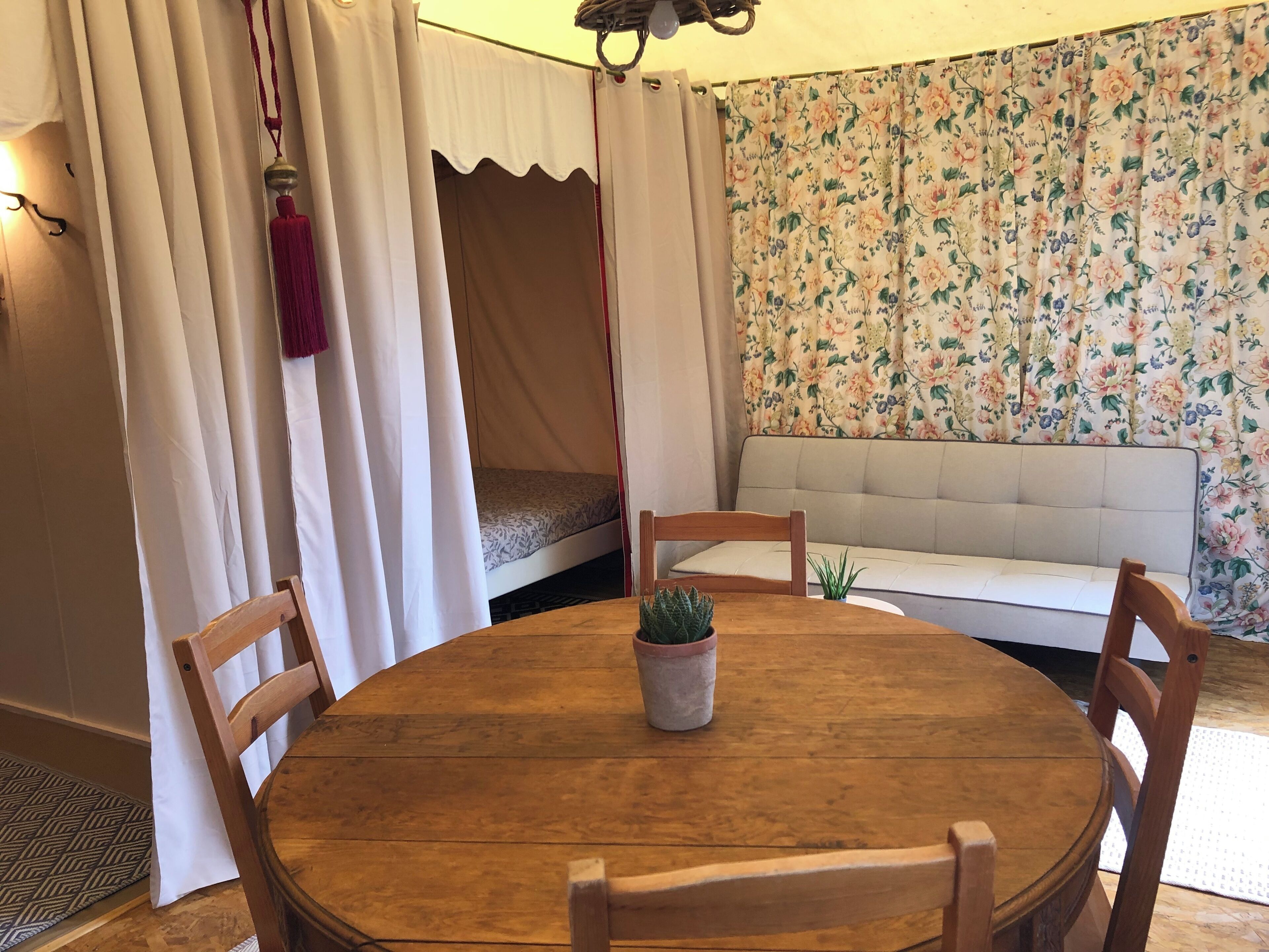 Una habitación acogedora con una mesa redonda de madera, dos sillas de madera, una planta pequeña en maceta, un sofá y una cama con dosel.