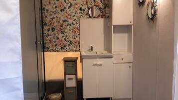Um banheiro com chuveiro, pia, espelho e armário.