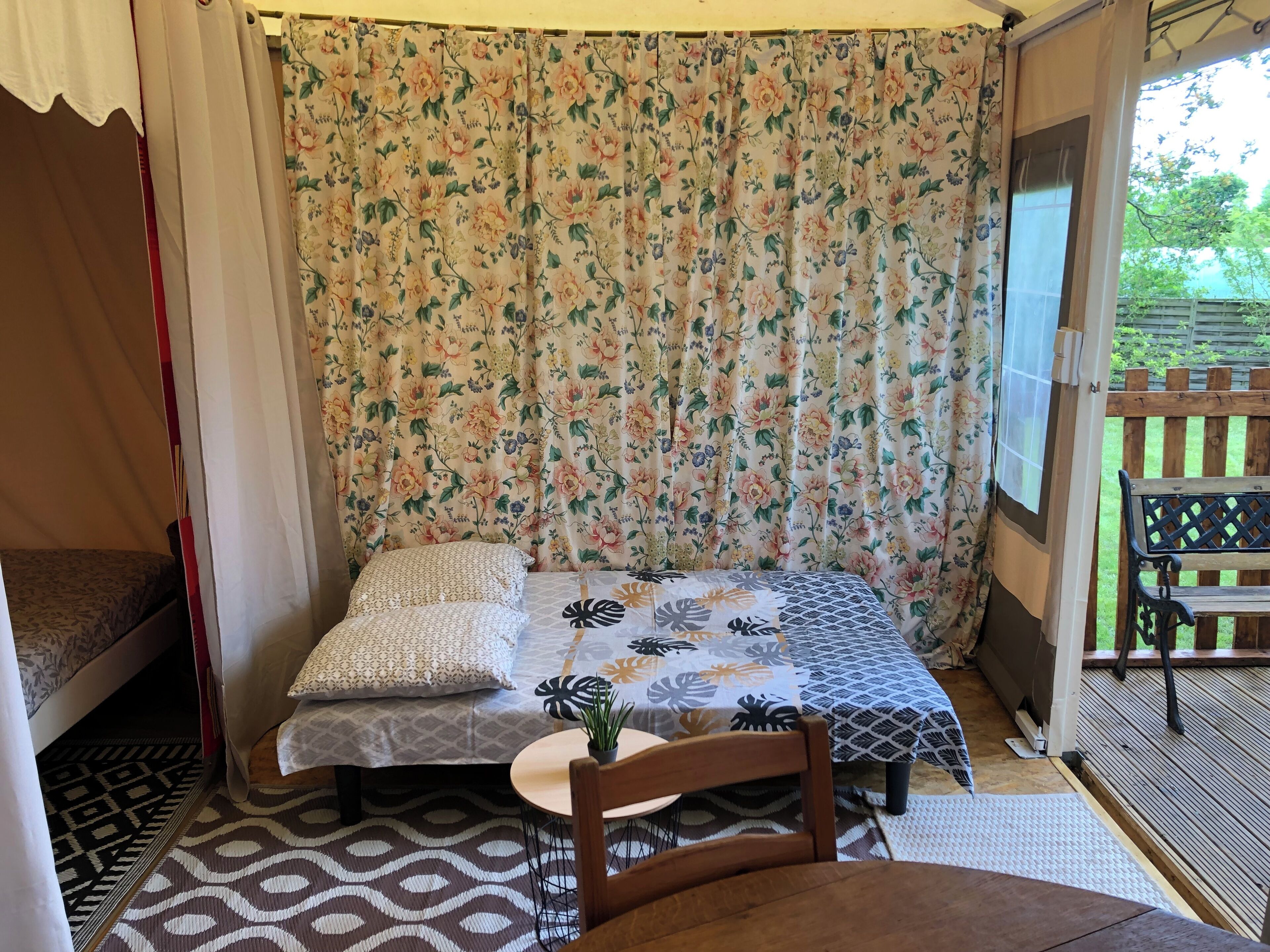 A cozy room with a bed, a small table with a plant, and a bench outside.