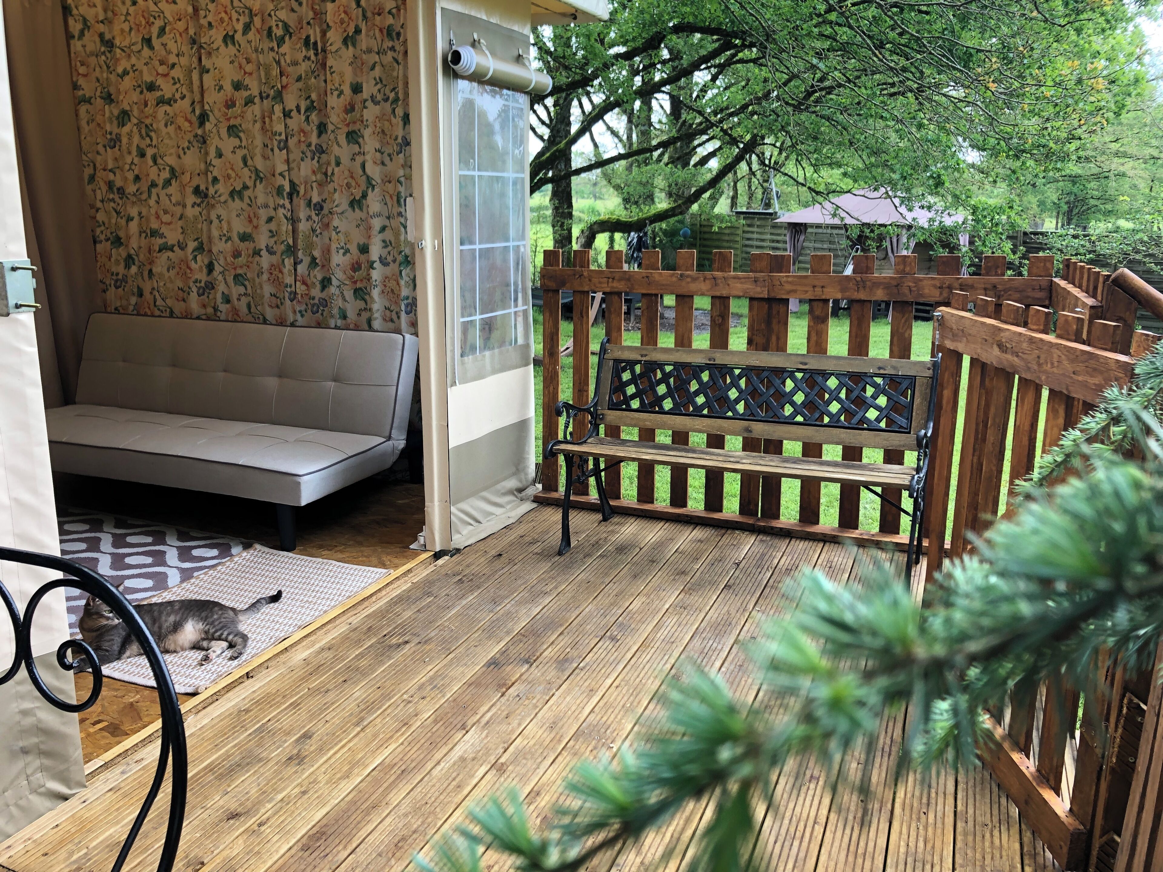 Una terraza de madera con un banco, un sofá y un gato.