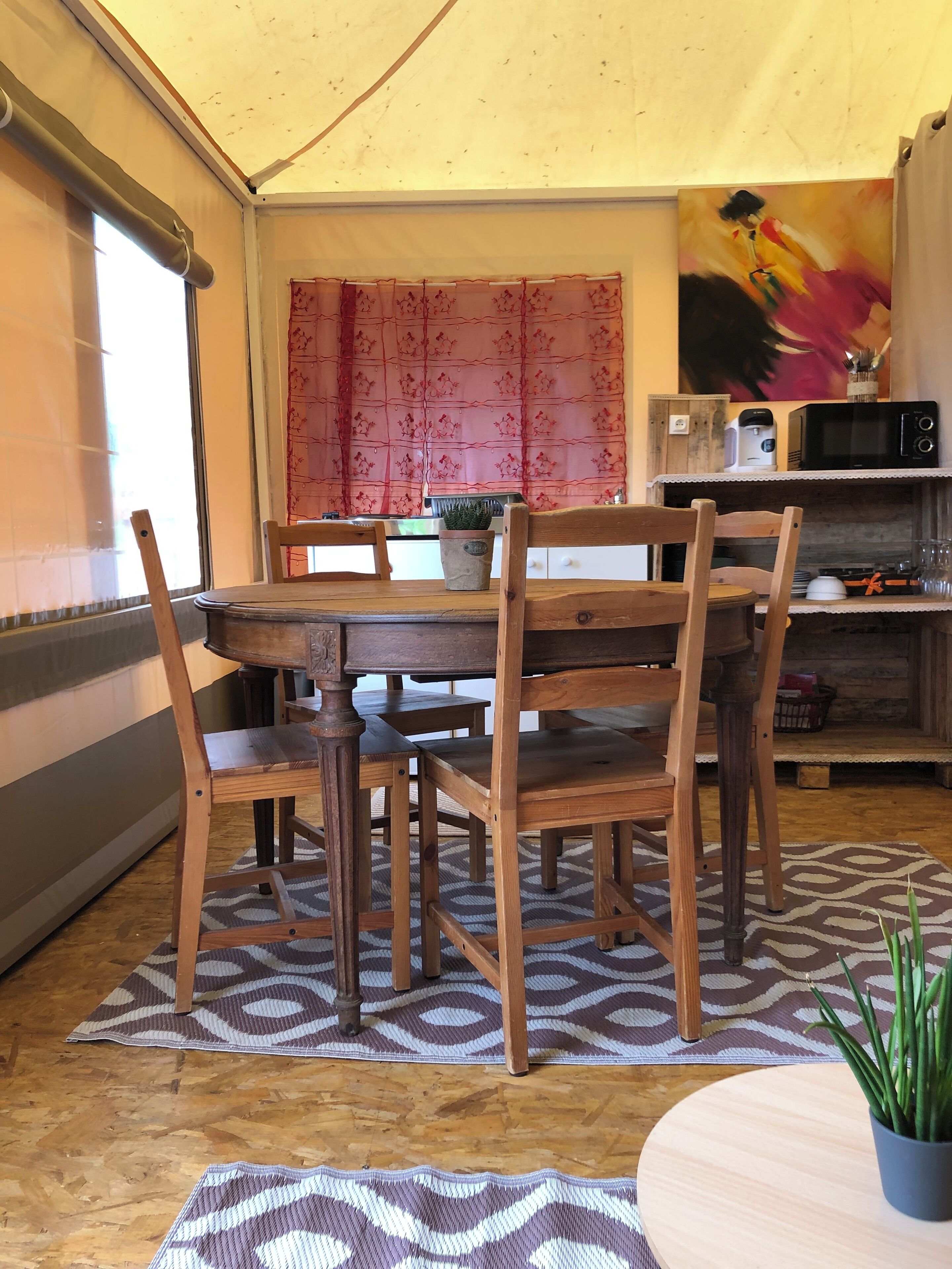 A dining area with a wooden table and chairs, a potted plant, and a kitchen area with a microwave and coffee maker.