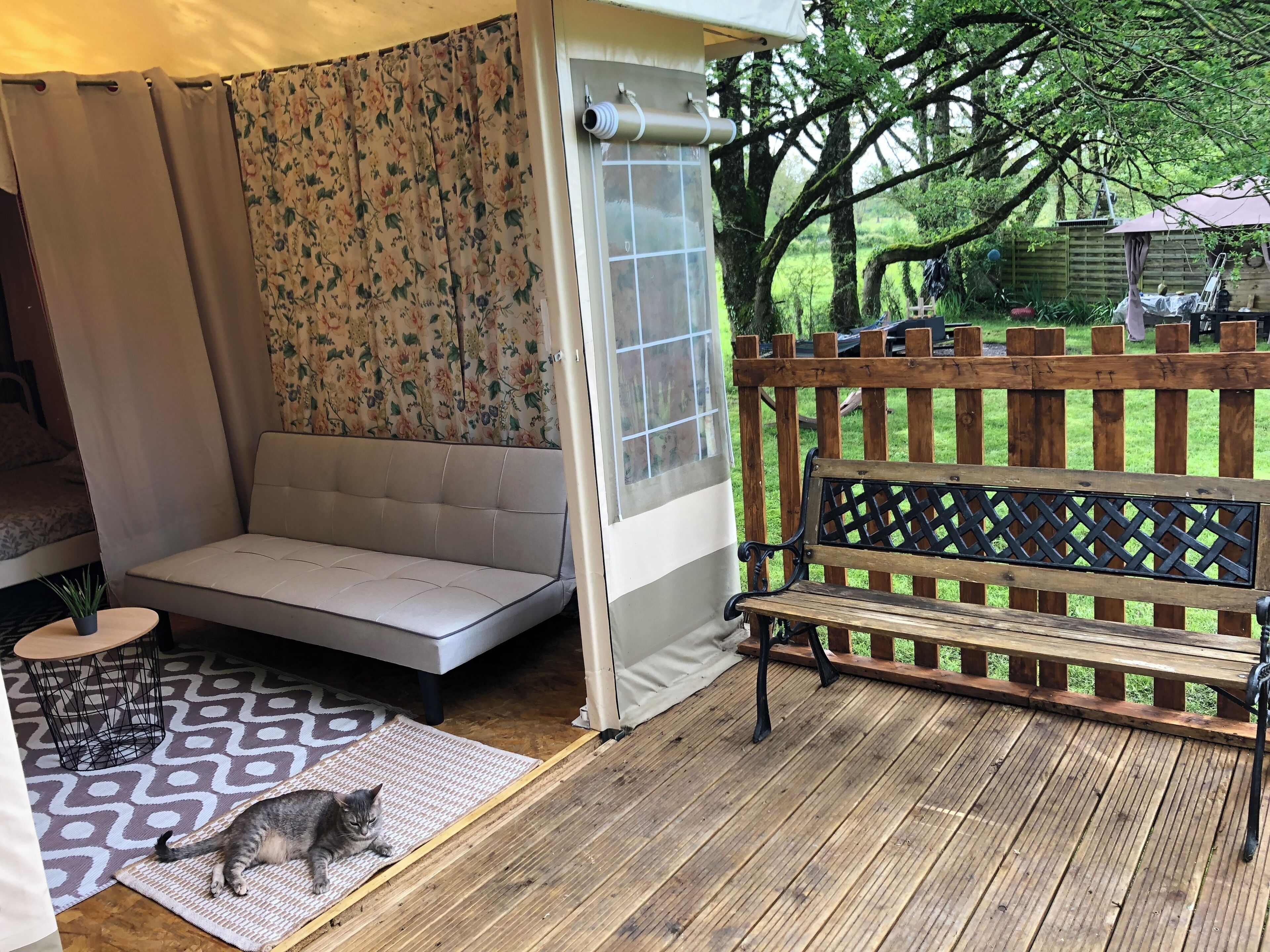 A covered patio area with a cushioned seating area, a wooden bench, and a potted plant.