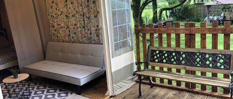 A covered patio area with a cushioned seating area, a wooden bench, and a potted plant.
