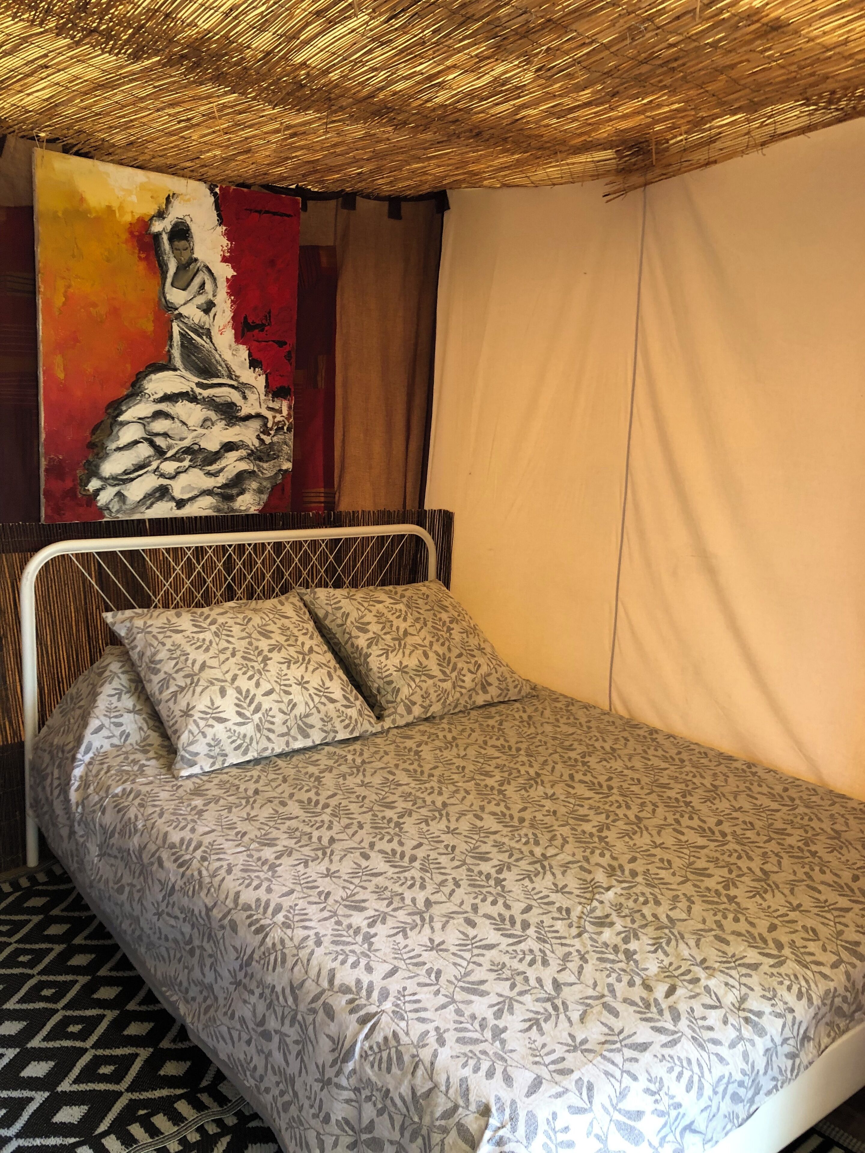 Un lit simple avec une couvre-lit à motifs, une tête de lit en métal et un mur orné d’un grand tableau abstrait.