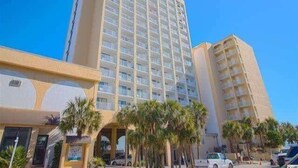 A multi-story hotel with a central atrium, palm trees, and a parking lot. - Oceanview Efficiency DW607 (Myrtle Beach)