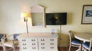 A hotel room with a TV, a dresser, two chairs, a table, a lamp, and a framed picture on the wall.