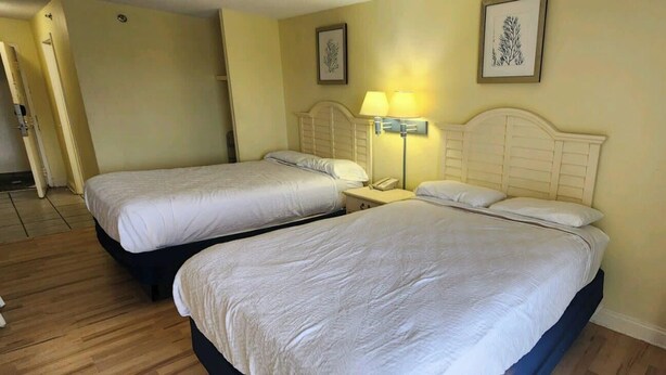 A hotel room with two beds, a nightstand with a lamp, a chair, and a door.