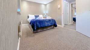 Una habitación de hotel con una cama, una mesita de noche, una lámpara y una puerta que da a otra habitación.