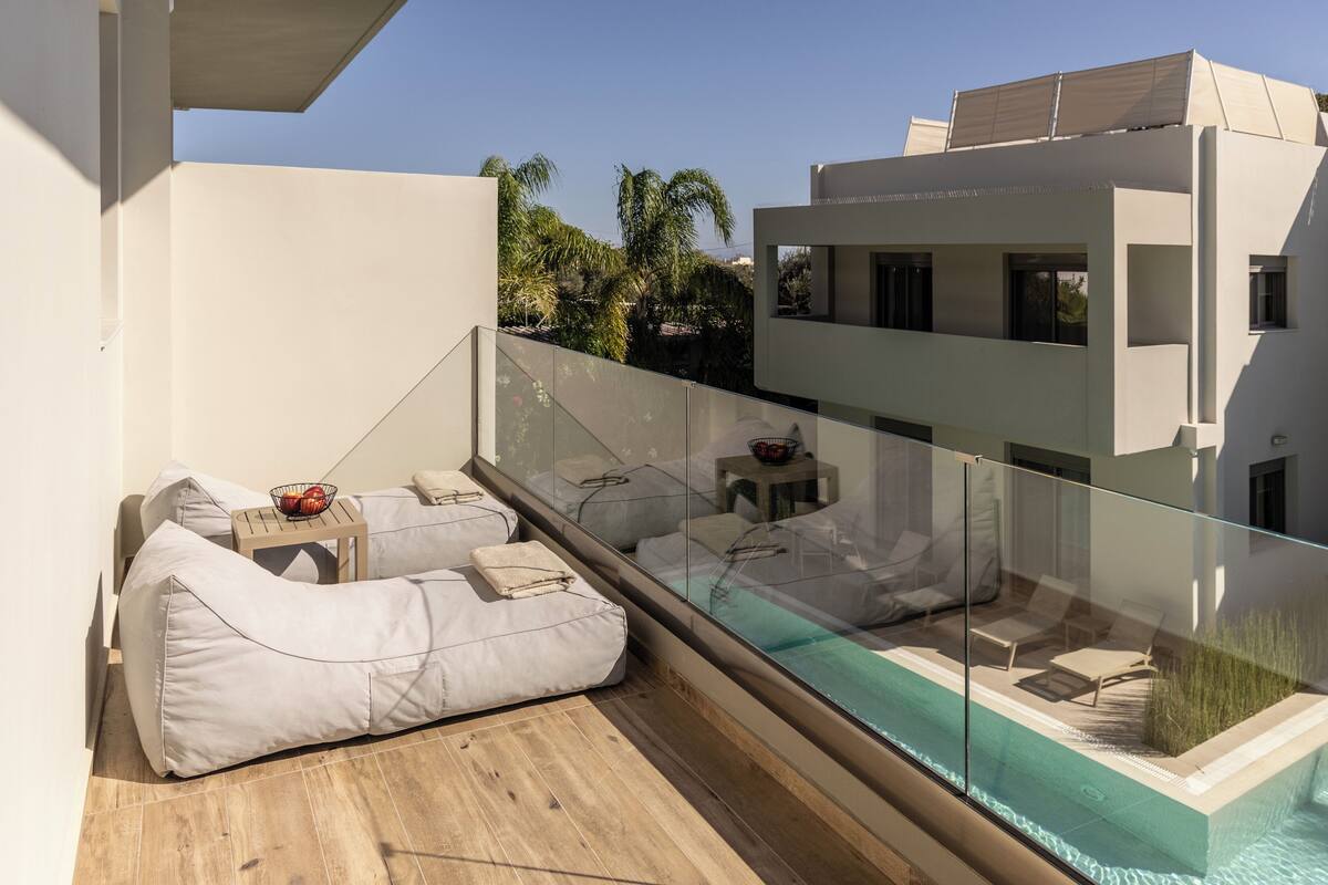 Un balcón moderno con barandilla de cristal, una zona de estar integrada y una piscina.