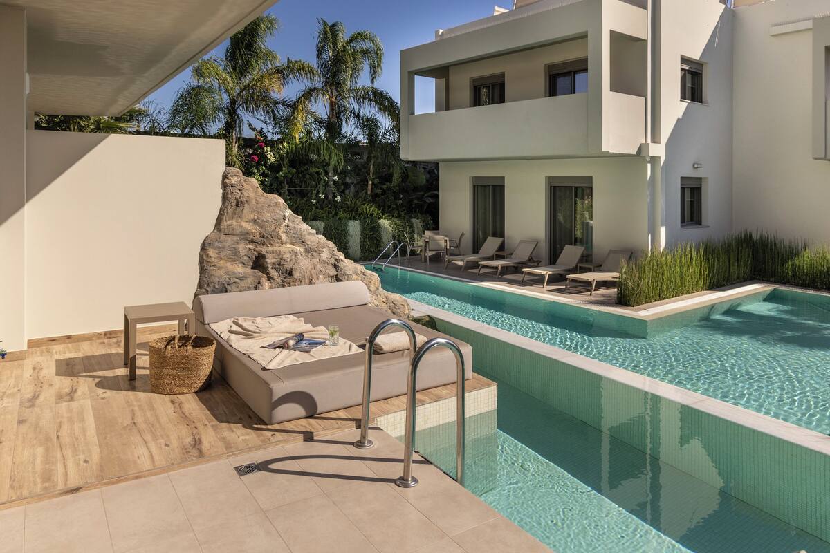 Un área de piscina moderna con una tumbona, una mesita y un elemento decorativo de piedra.