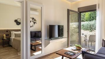 A modern living room with a sofa, a coffee table, and a TV on a glass shelf. There is a sliding glass door leading to an outdoor area with a table and chairs.