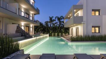 A modern pool area with lounge chairs, a rock feature, and a well-lit building in the background.
