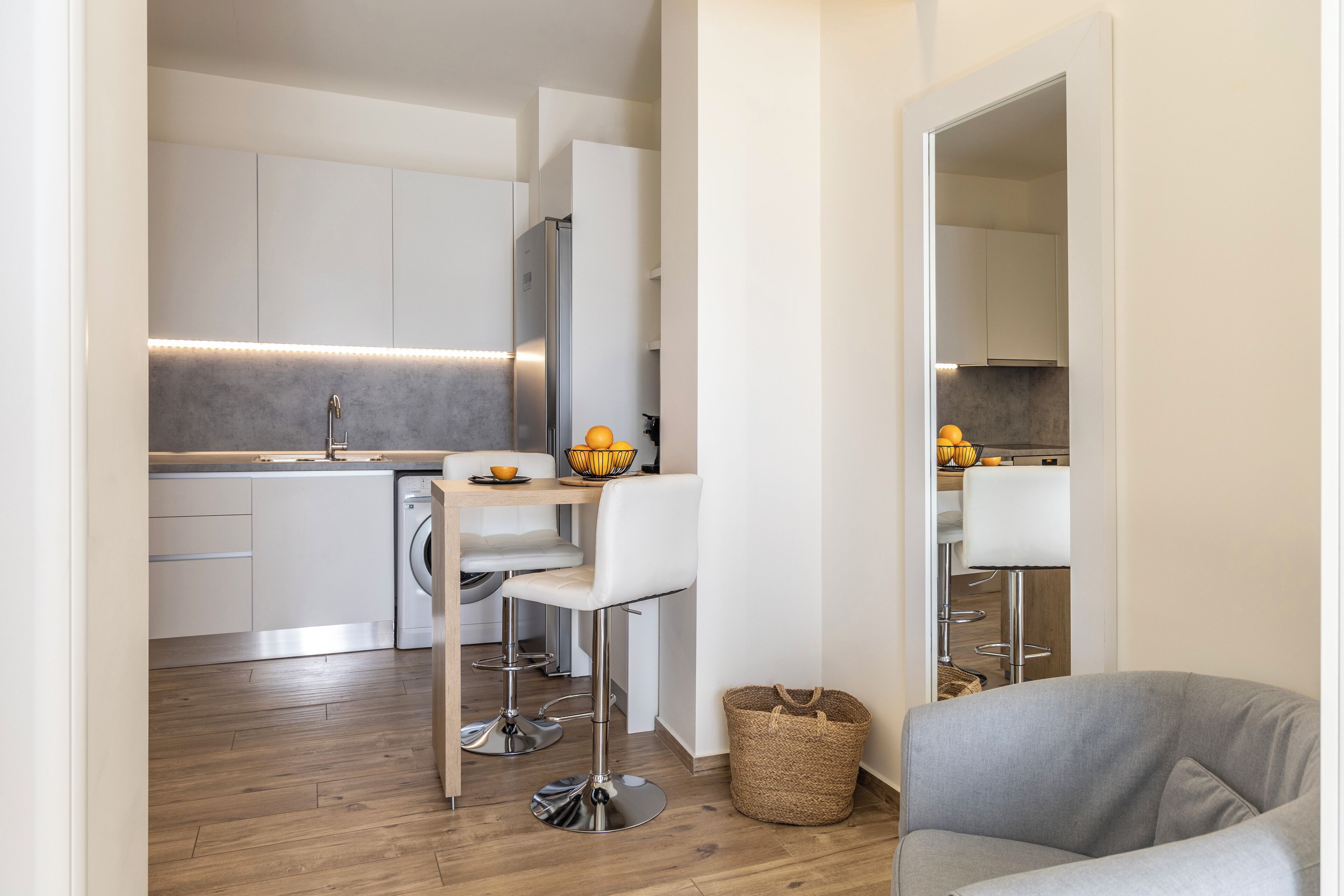 A modern kitchen with white cabinets, stainless steel appliances, and a wooden floor.