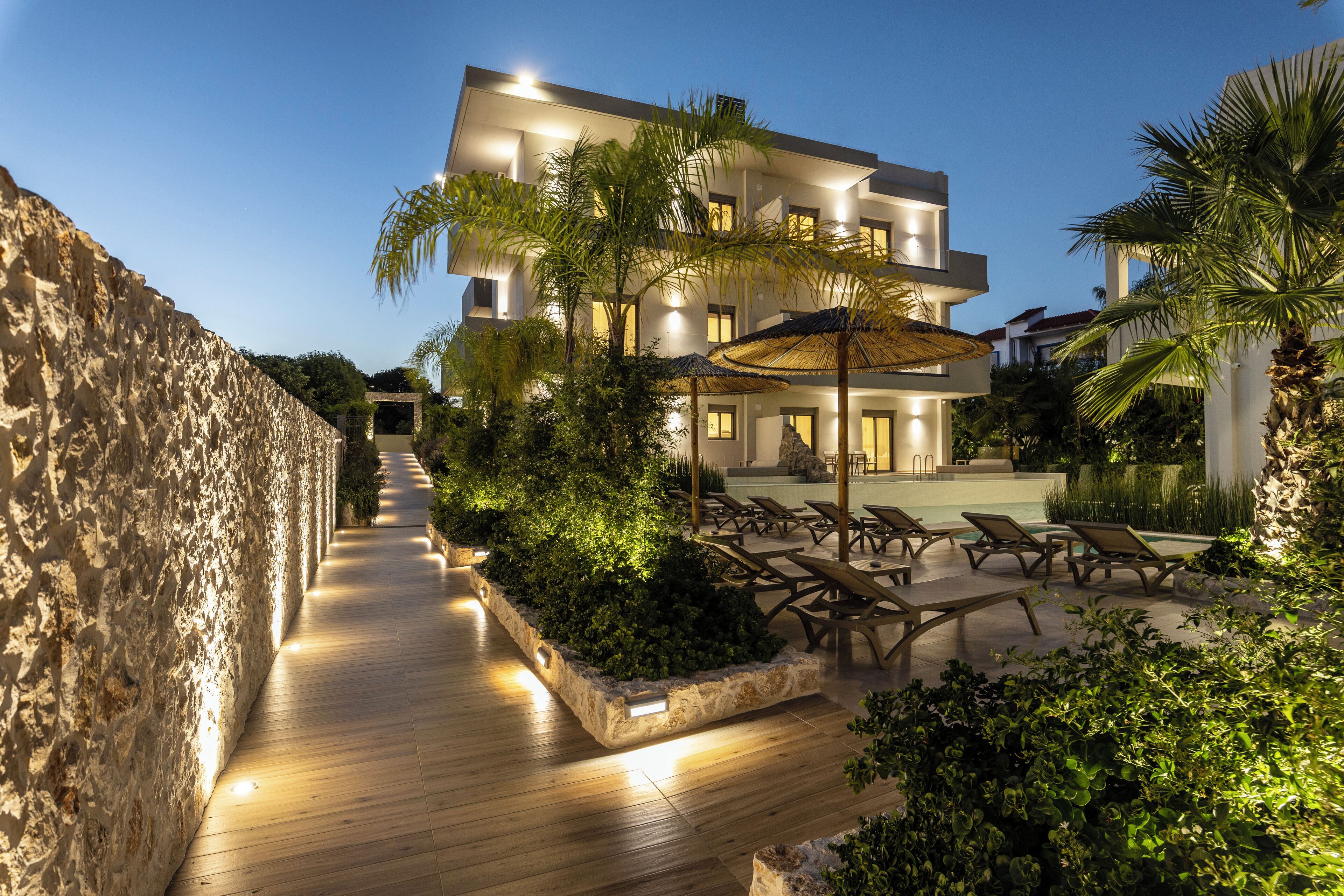 A modern building with a pool area, lounge chairs, and a stone wall.