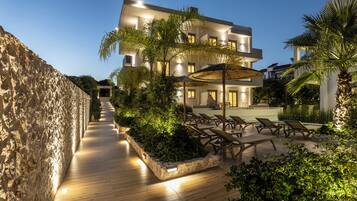 A modern building with a pool area, lounge chairs, and a stone wall.