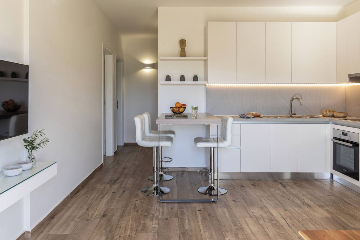 Una cocina moderna con armarios blancos, horno empotrado y una zona de bar con taburetes.
