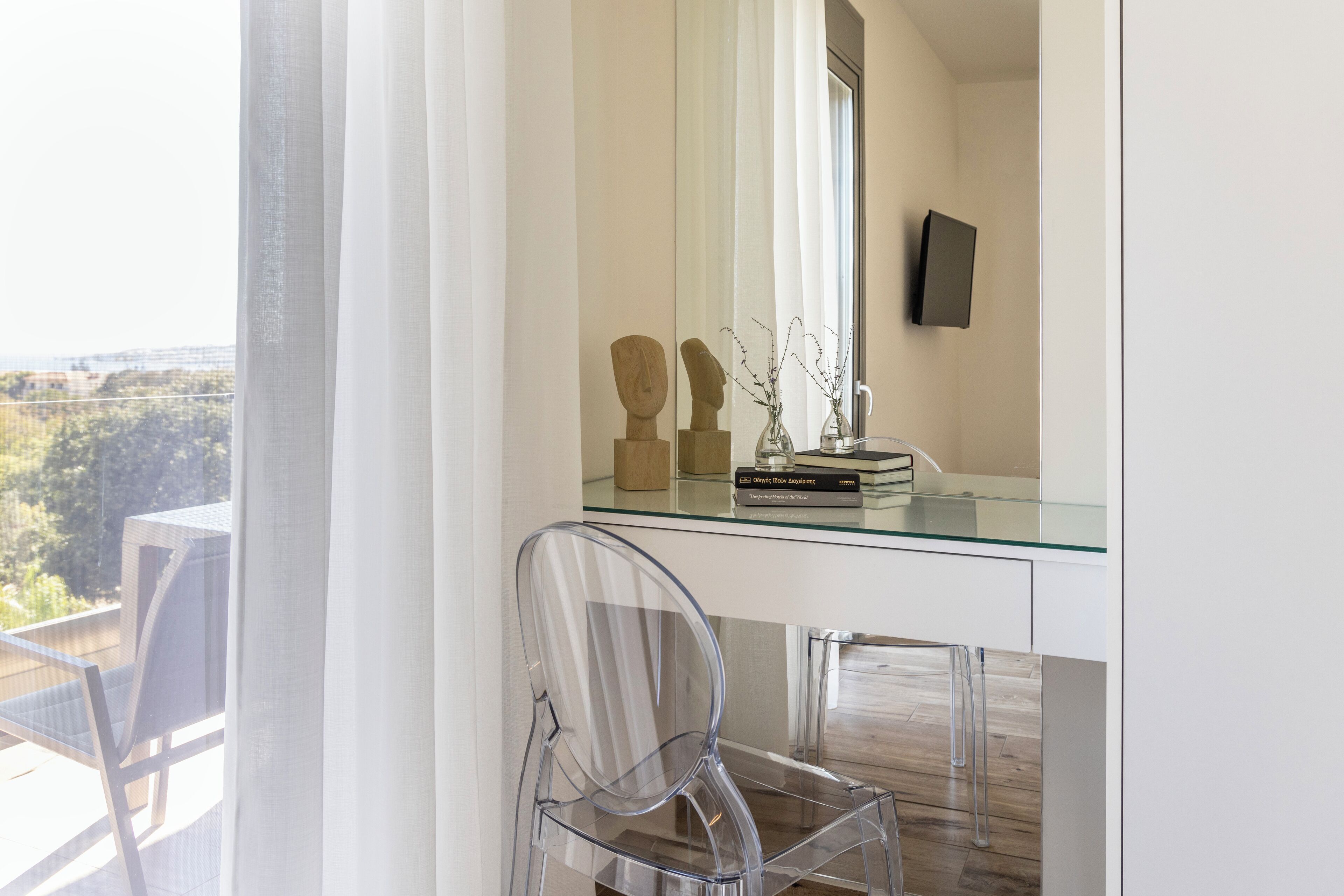 A modern room with a glass desk, clear chair, and a view of the outdoors.