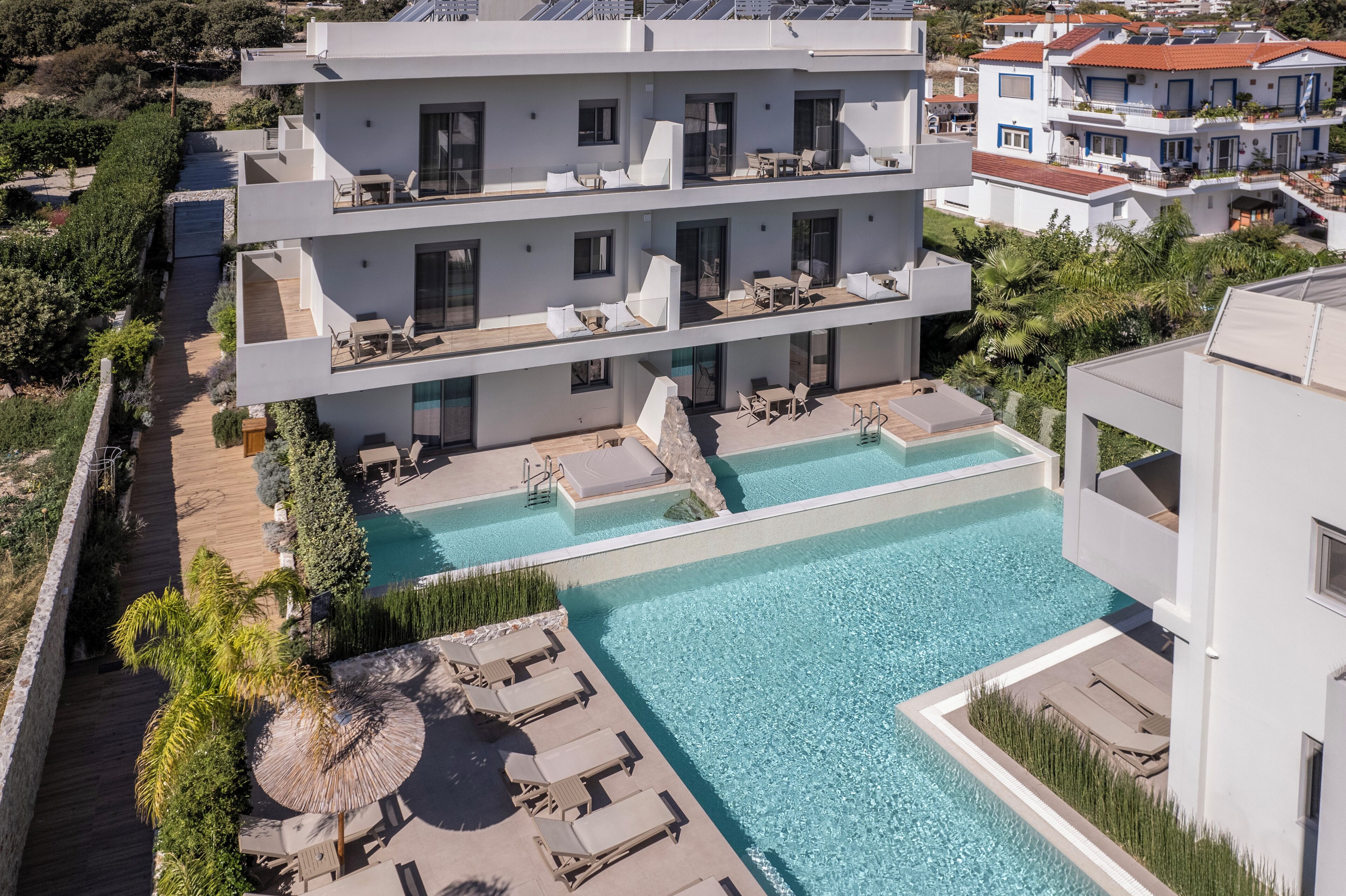 Un hotel moderno de varios pisos con una zona de piscina en la azotea, que incluye tumbonas y una pequeña zona de estar circular.