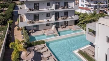 Un hotel moderno de varios pisos con una zona de piscina en la azotea, que incluye tumbonas y una pequeña zona de estar circular.