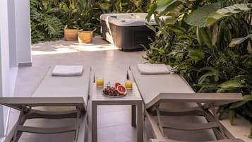 Relax in a serene outdoor setting with a long table for dining or socializing, surrounded by lush tropical plants and a hot tub.