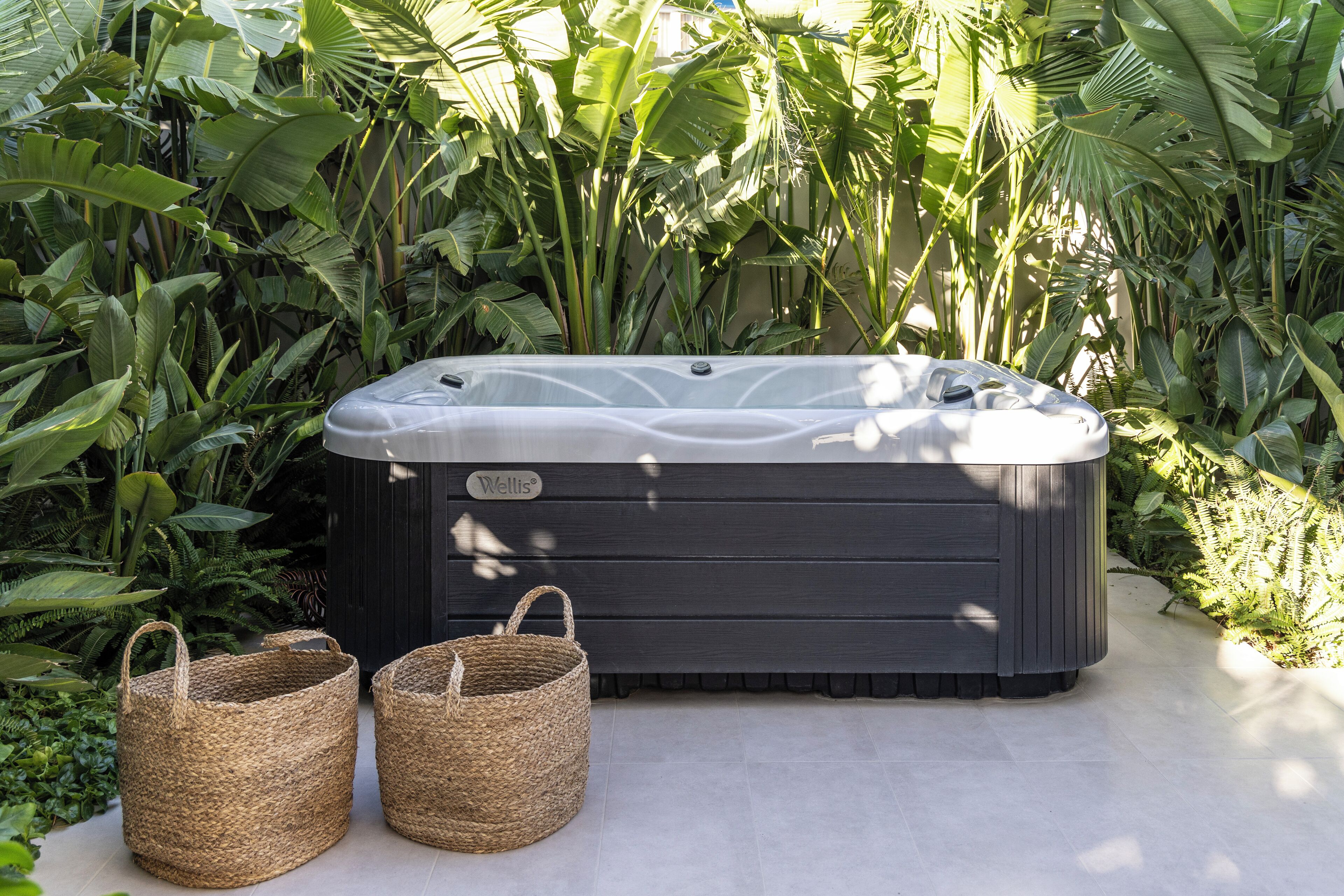 Ein Whirlpool, umgeben von üppigem Grün, mit zwei gewebten Körben davor.